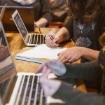stock image of a computer coding workshop with female hands visible and computers, no faces