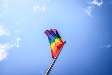 LGBTQ flag blowing in the wind before a blue sky