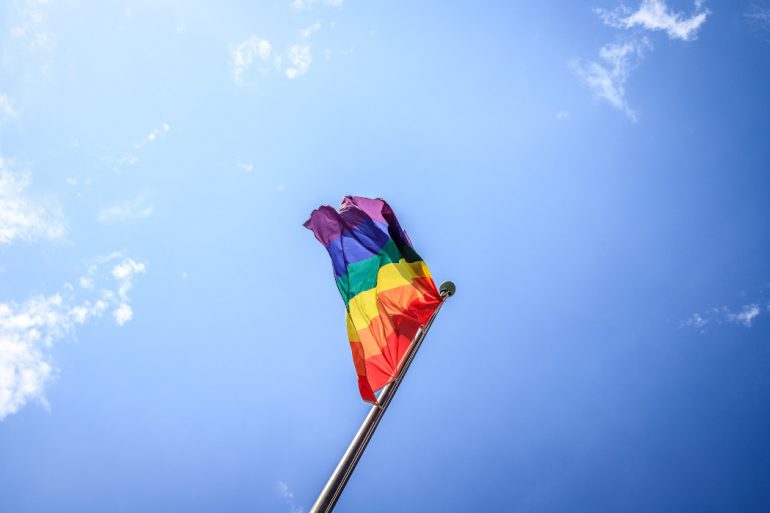 LGBTQ flag blowing in the wind before a blue sky