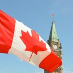 Canadian flag flies in the foreground over the parliament buildings in Ottawa on a sunny day