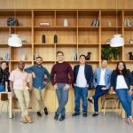 Employees at Perch standing next to each other in front of a wall of wooden shelves.