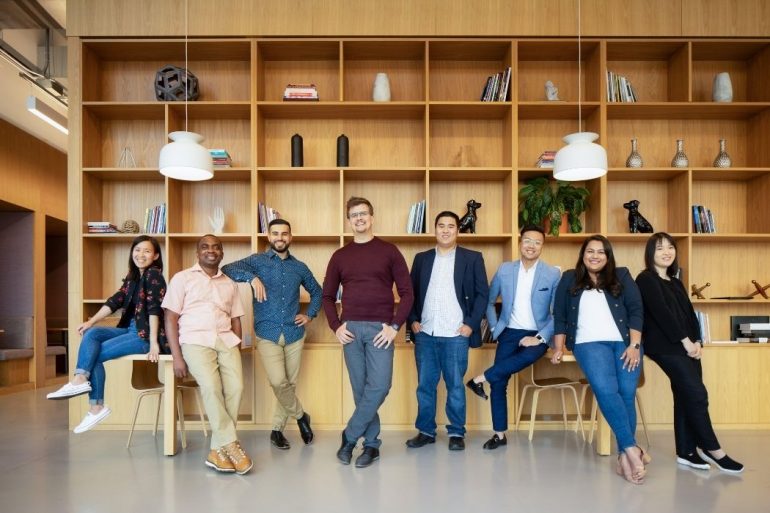 Employees at Perch standing next to each other in front of a wall of wooden shelves.