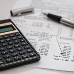 A black calculator and a sheet of white paper with financial statements on top of a white surface.