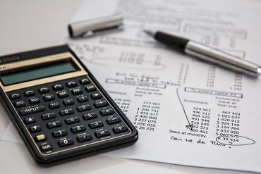 A black calculator and a sheet of white paper with financial statements on top of a white surface.