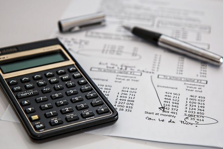 A black calculator and a sheet of white paper with financial statements on top of a white surface.