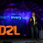 D2L founder John Baker standing on a stage with the D2L logo behind him