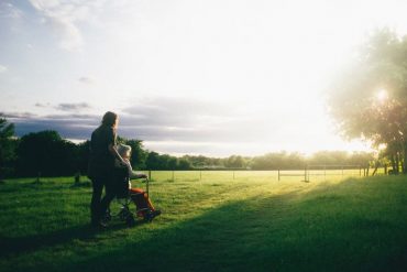 Caregiver with an elderly person in a wheelchair looking out into the open field of grass