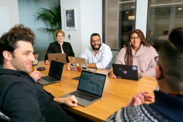 People sitting around a desk with their laptops open