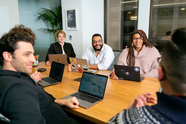 People sitting around a desk with their laptops open