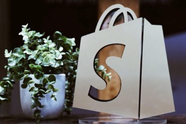 Shopify logo bag beside a green plant.
