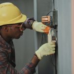 an electrician wearing a yellow helmet installs a switch on a wall in a commercial building