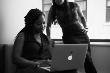 Black and white image of two women looking at a macbook.