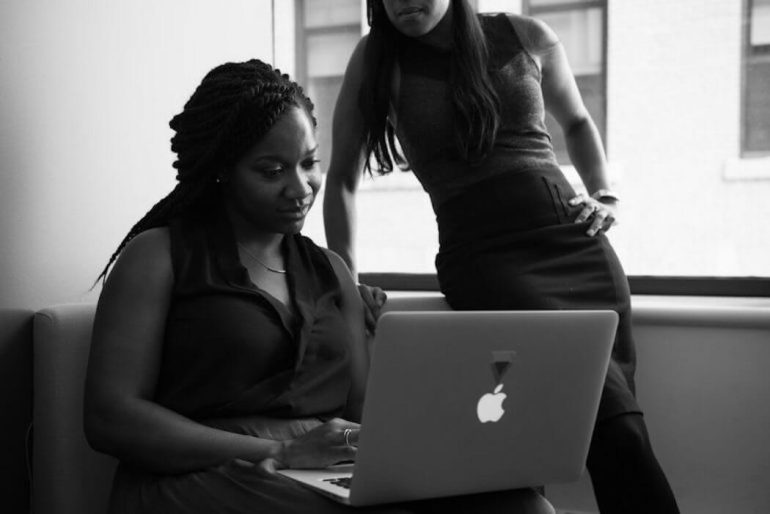 Black and white image of two women looking at a macbook.
