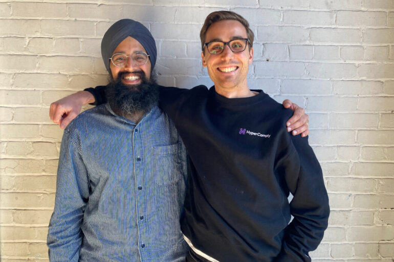 HyperComply co-founders Amar Chahal and Cody Wright stand with their arms around each others' shoulders.
