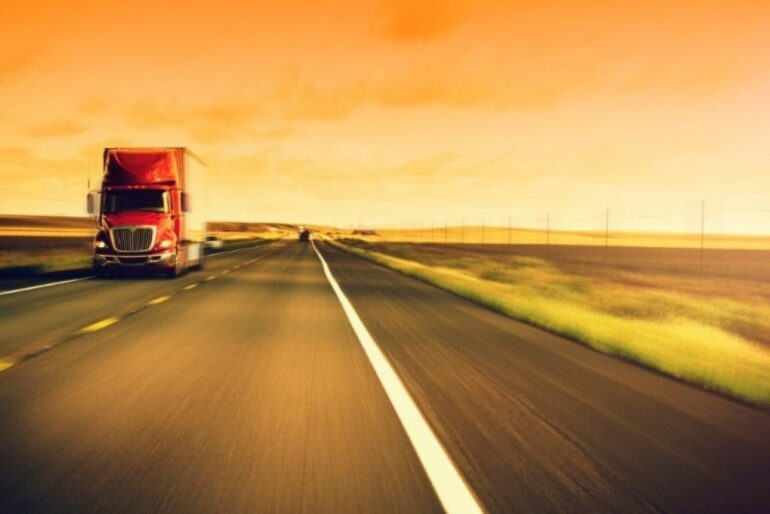 a red transport truck driving toward the camera with an orange tinted backdrop