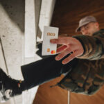 a man in skateboard shoes leans sideways and flashes a Neo mastercard at the camera. it is in focus in the foreground and he is out of focus in the background