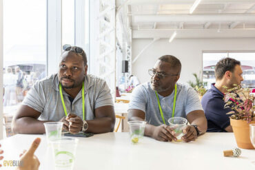 Two men wearing lanyards sit at a table with plastic cups in front of them at a past startupfest event