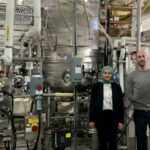 A woman and man stand in front of one of Ardra's large industrial fermenters