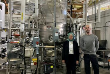 A woman and man stand in front of one of Ardra's large industrial fermenters