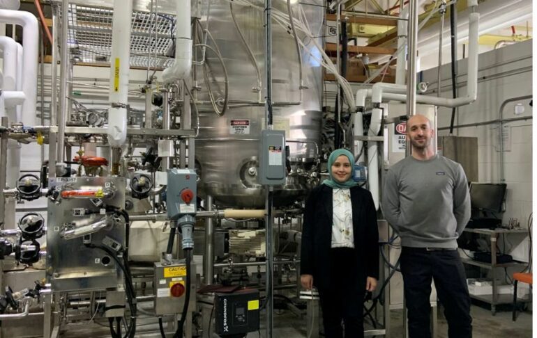 A woman and man stand in front of one of Ardra's large industrial fermenters