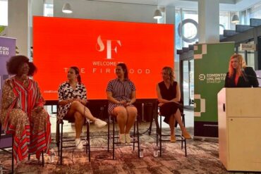 Four women speak on a panel with a red backdrop that says The Firehood