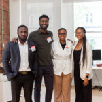 four staff members from Tribe, people of colour pose for a picture at an office with exposed brick walls
