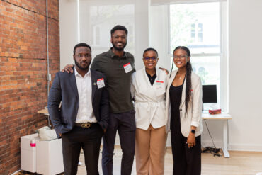 four staff members from Tribe, people of colour pose for a picture at an office with exposed brick walls