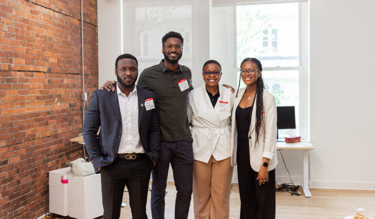 four staff members from Tribe, people of colour pose for a picture at an office with exposed brick walls