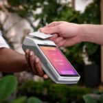 someone taps a payment card on a handheld terminal with a pink user interface on the screen