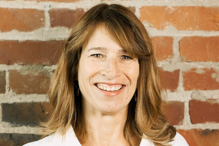 A smiling headshot photograph of Monique Morden with a brick wall backdrop