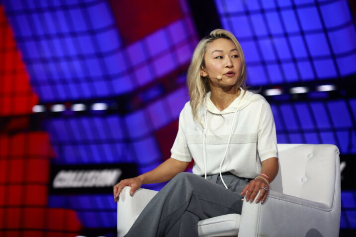 Sarah Guo sits in a chair on stage with a mic on her face on a panel at Collision