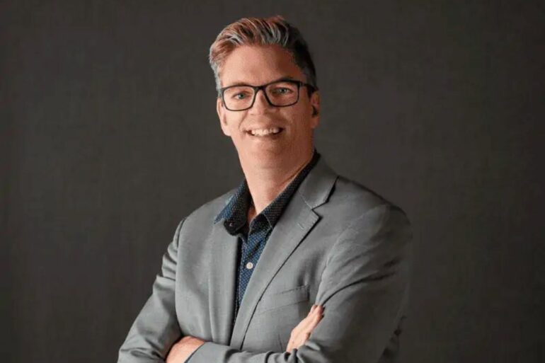 portrait of Darrell Petras on a plain grey background. he wears a suit and black eyeglasses.
