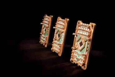 three quantum processors, which look like small circuits in a bronze colour, displayed on an angle on a black background
