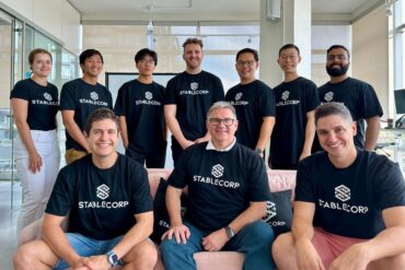 staff portrait in office with about a dozen people in navy stablecorp t shirts