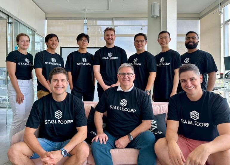 staff portrait in office with about a dozen people in navy stablecorp t shirts