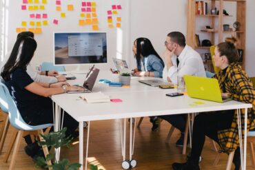 Five people at table watching screen of white computer monitor
