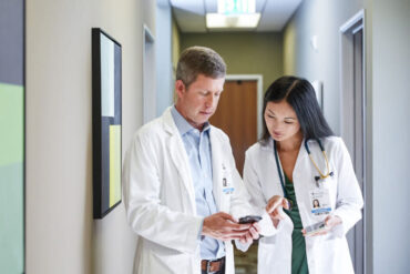 Two doctors look at a cell phone in hallway
