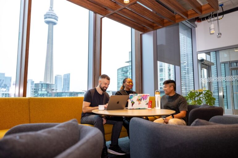 A group of people work at a small table with the CN tower in view through the windows behind them