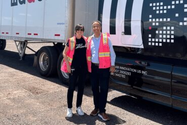 Two people in fluorescent vests stand in front of trucks