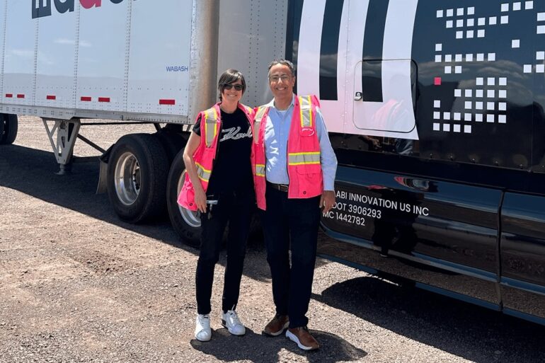 Two people in fluorescent vests stand in front of trucks