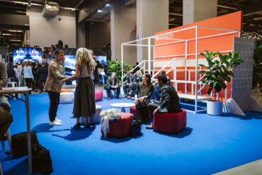 People sit and stand in front of Cohere's booth at the 2025 ALL IN conference.