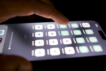 A hand hovers above a smartphone that displays several Ai apps on the screen.