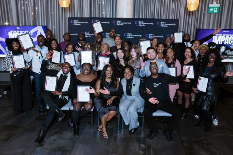 A large group of Black entrepreneurs sit together, smiling at the camera
