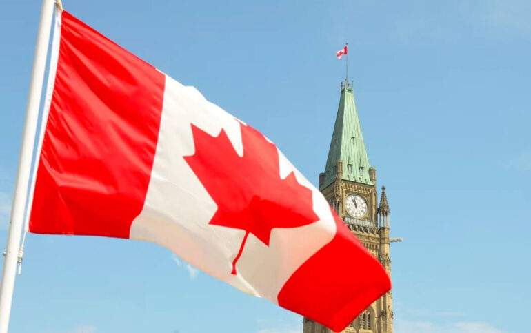 The Canadian flag blows in the wind with Parliament hill in the background