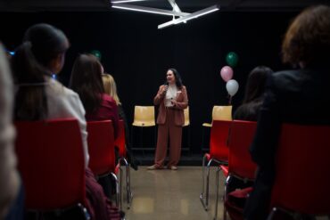 A woman holding a mic speaks to a seated audience.