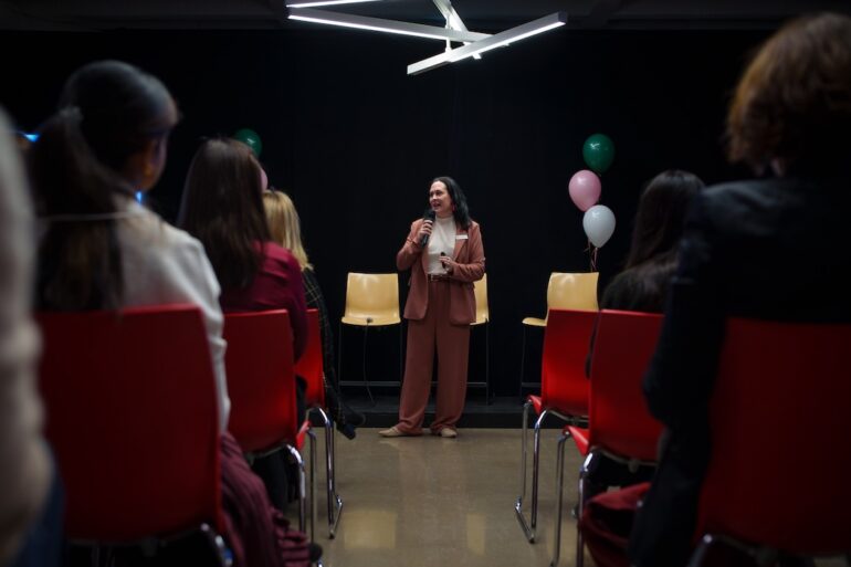 A woman holding a mic speaks to a seated audience.