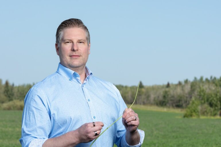 Marek Hejduk stands in a green field, holding a green sprig in his hands.