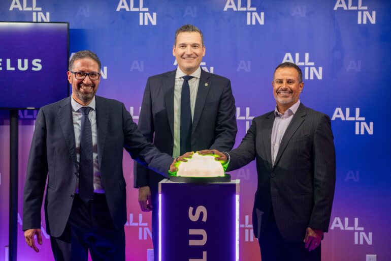 Evan Solomon stands on stage with two other men in suits. They are pressing a novelty-sized green button.
