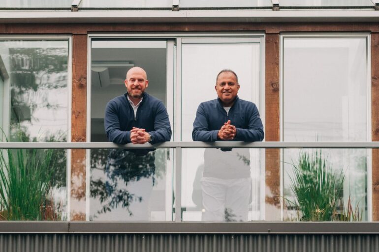Noah Shipman and Randy Garg lean against the railing of a balcony, facing the camera.
