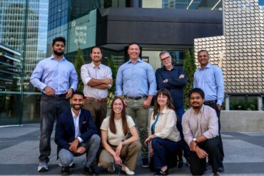 Nine people post in front of an office building